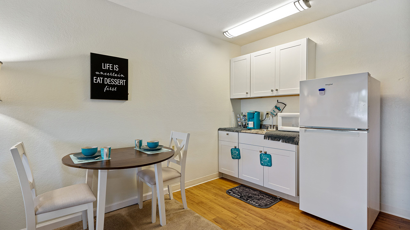 Senior apartment kitchenette with white cabinets and appliances and dinette for two set with teal tableware at Holiday Summerfield Estates.