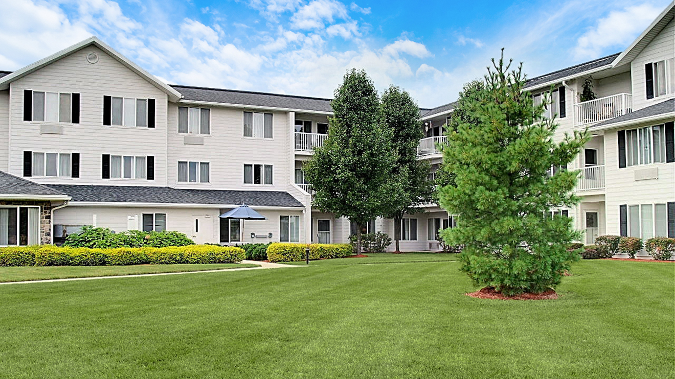 Three-story senior apartment building exterior with balconies and lush grounds to explore.