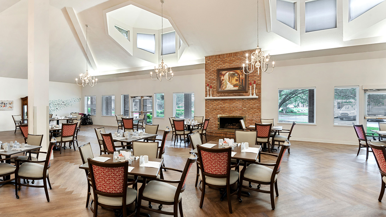 Airy retirement community dining room with brick fireplace and tables for resident gatherings.