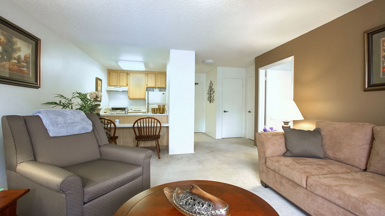 Senior apartment living room with furniture and a kitchen with breakfast bar at Holiday Springs of Escondido.