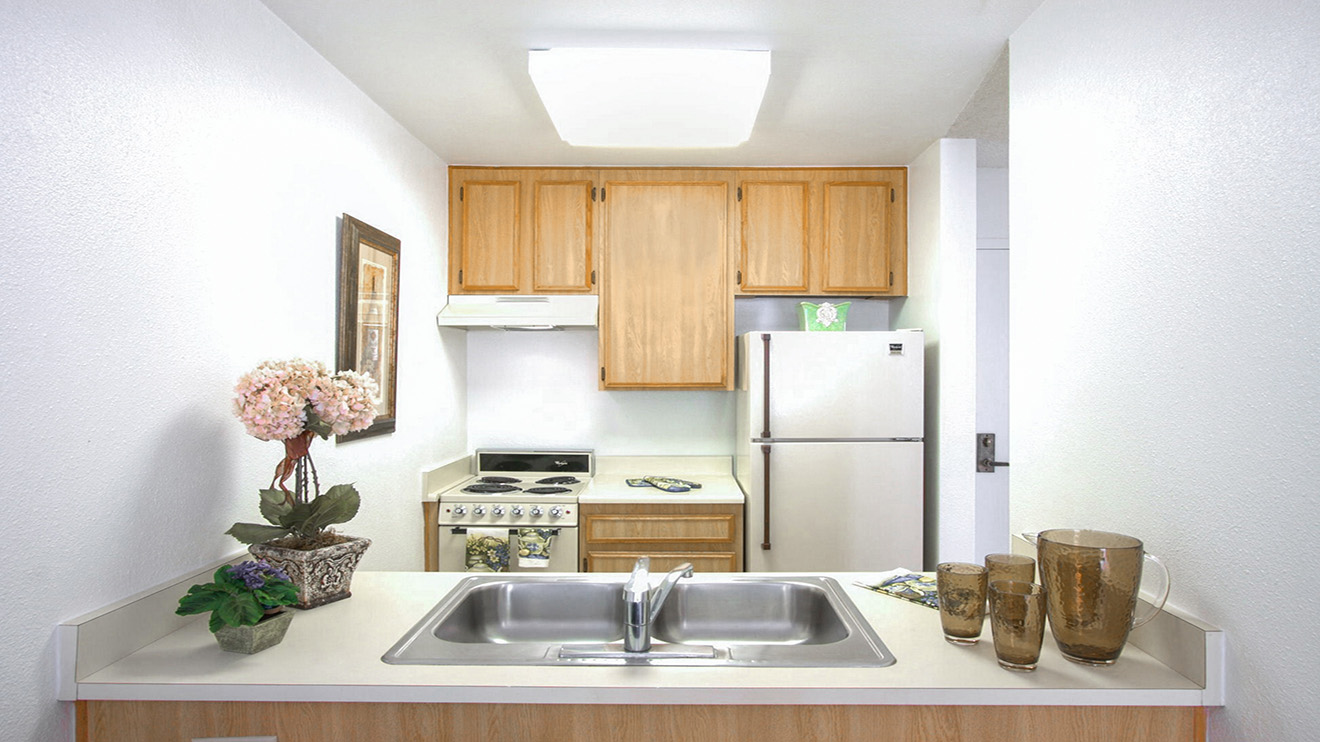Holiday Springs of Escondido senior apartment kitchen with stove, refrigerator and sink with overhead lighting.